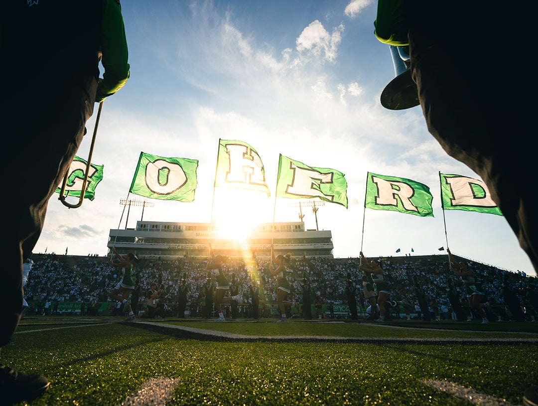 Flags spell out 'Go Herd' from the football field with the Marshall University press box in the background.