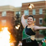 A Marshall University majorette twirls a flaming baton during an outdoor performance.