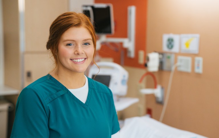 female nursing student in scrubs smiling at the camera in a hospital room