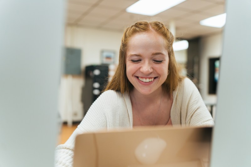 student looking at a laptop and smiling at it