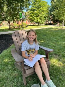 a girl sitting in a chair outside writing in a notebook