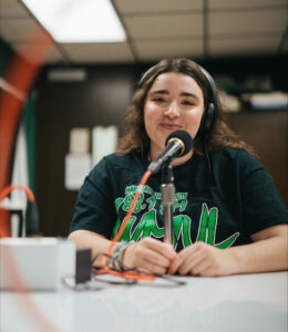 Emma Johnson wears headphones and speaks into a microphone in Marshall University's WMUL radio studio.