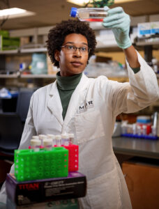 Sidney Strause wears her white coat while she looks at a bottle of liquid in a lab