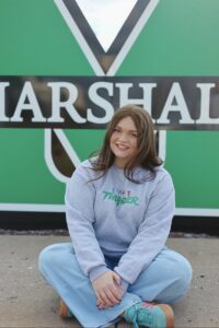 Emily Price sits smiling in front of a large Marshall sign