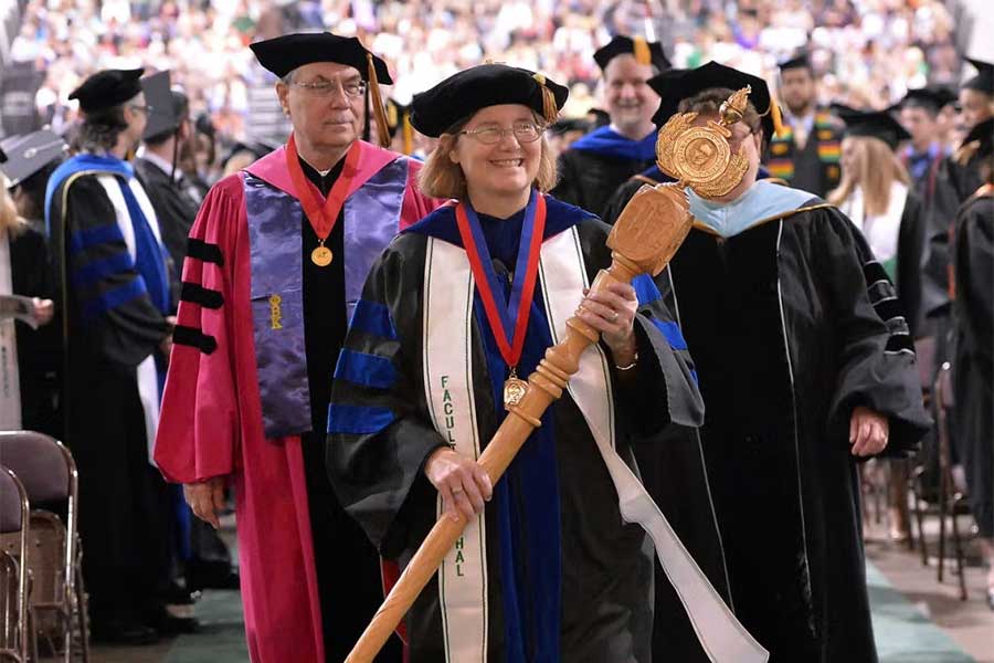 Faculty grand marshal leads a graduation procession while carrying the ceremonial Grand Mace, a symbol of Marshall University authority and tradition.
