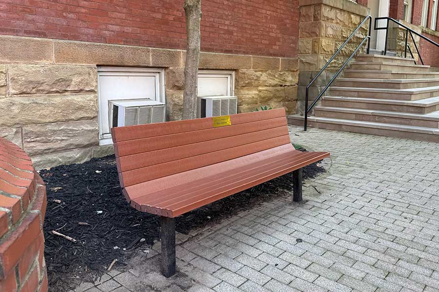 Memorial bench outside Old Main with a plaque honoring Hal Shaver, positioned beside the historic building's brick facade and entrance steps.