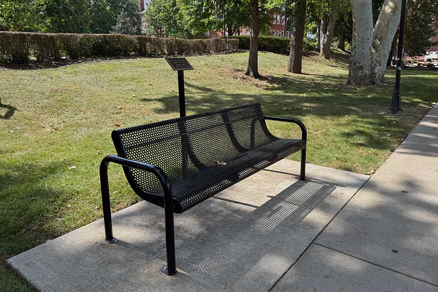 Memorial bench south of Morrow Library honoring Terry Lovely Snowder, positioned along a campus walkway beneath mature shade trees near hammocks and outdoor seating areas.
