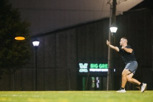 Student throws a flying disc on a lighted recreation field at night on Marshall University’s campus.