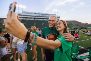 Student takes a selfie with a university representative on the football field during a campus gathering at Marshall University.